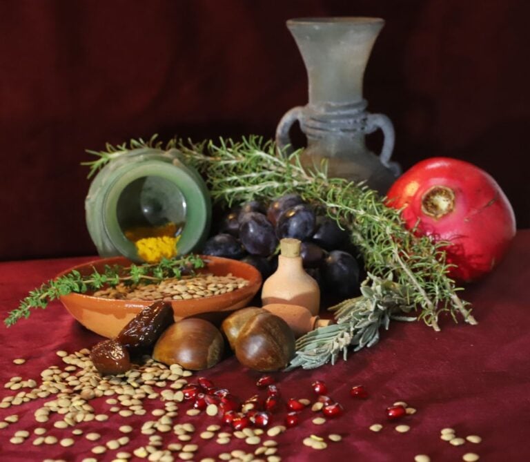 Imagem de uma natureza morta onde vemos castanhas, tâmaras, uvas, feijões, sementes de romã e uma romã