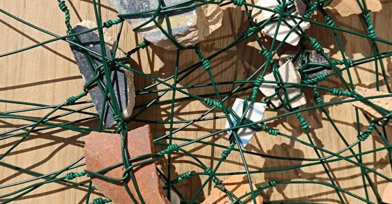 Imagem de vários fragmentos de barro embrenhados numa teia de arame verde